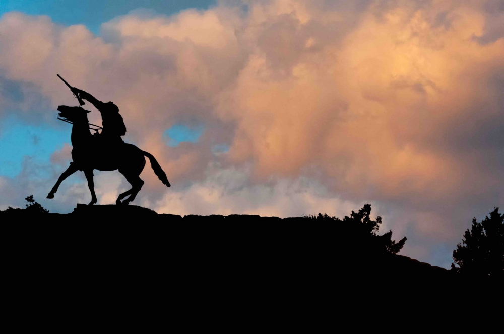 a sunset photo of a statue portraying Buffalo Bill Cody on a bucking horse that is featured proudly in Cody Wyoming